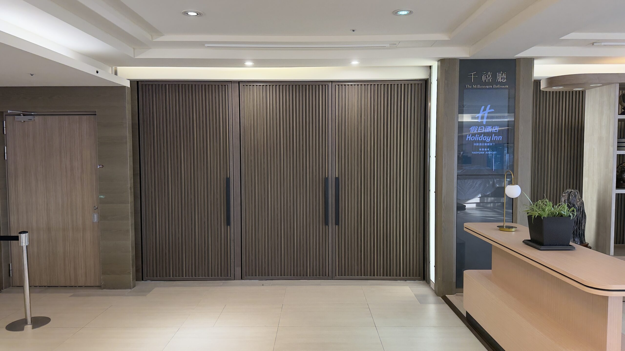2025台灣第一家Holiday Inn Taoyuan Airport桃園機場假日酒店開箱|鄰近 Xpark、華泰名品城,旅遊搭機都方便 19 Hotel lobby area of Holiday Inn Taoyuan Airport featuring wooden paneling, a reception desk, and a sign for the Millennium Hall.